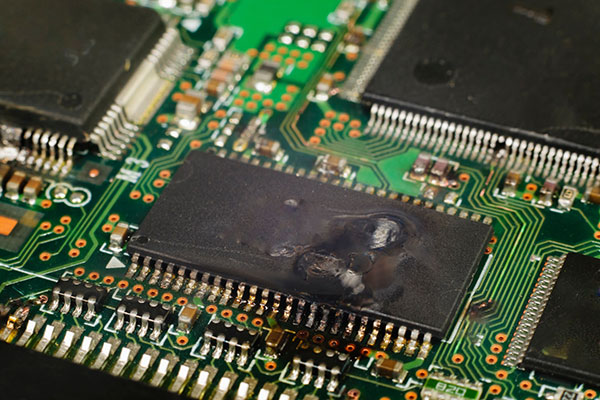 静電気放電（ESD）よってPC内部の基板上のICが焼損した写真。ICの天面が焼けて白化し、リードやプリント基板の一部が焼けて黒ずんだ外観。
